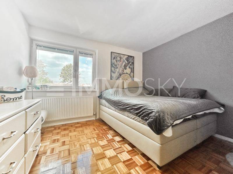 Gemütliches Schlafzimmer mit Doppelbett, weißer Kommode und Parkettboden, hell durch das Fenster.