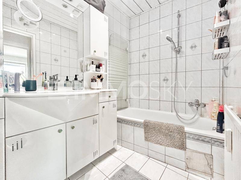 Helles Badezimmer mit weißen Fliesen, Badewanne mit Duschfunktion und einem praktischen Spiegelschrank.