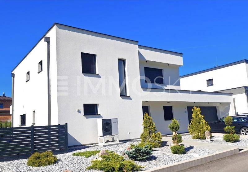 Seitliche Ansicht des modernen Hauses mit Garage, Vorgarten und Wärmepumpe.