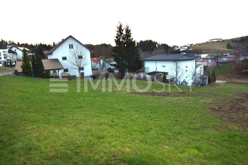 Großzügige Rasenfläche mit zwei Wohnhäusern im Vordergrund und dem Dorf am Horizont.