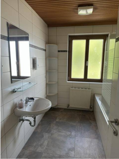 Helles Badezimmer mit Badewanne, Waschbecken und Holzdecke, ausgestattet mit einem Fenster.