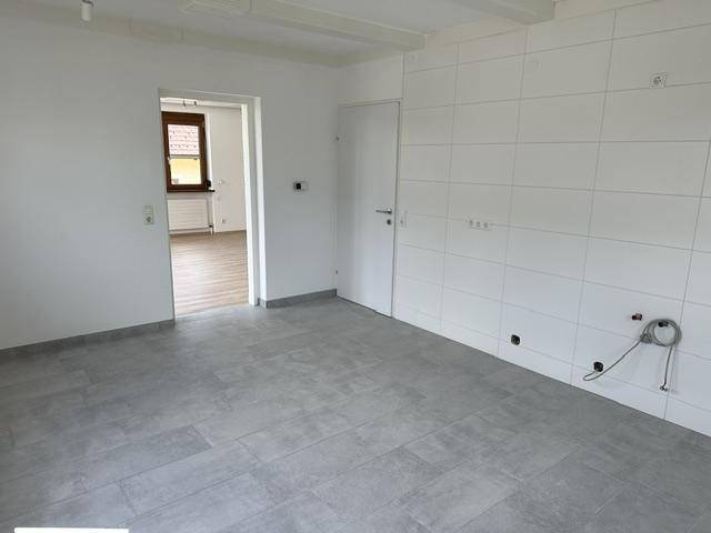 Heller Raum mit grauen Fliesen und weiß gefliester Wand, vorbereitet für eine Kücheninstallation.