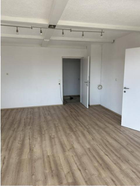 Geräumiger, heller Raum mit Laminatboden, weißen Wänden und sichtbaren Deckenbalken.