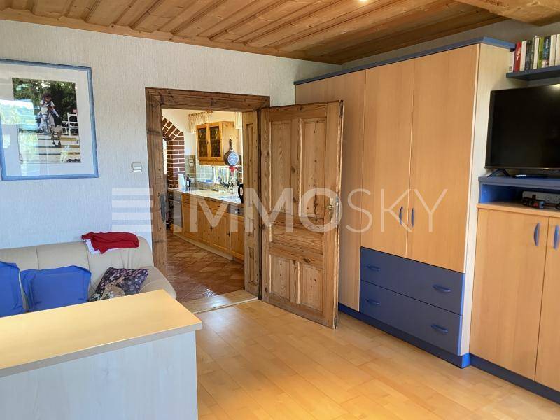 Gemütliches Wohnzimmer mit Holzboden und -decke, Blick in die angrenzende Küche.