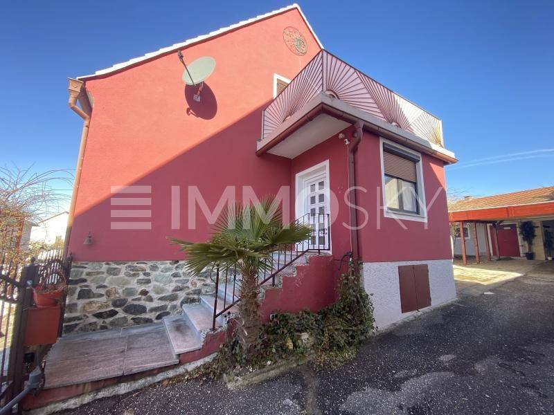 Rotes Haus mit Steinsockel, Außentreppe und Satellitenschüssel unter blauem Himmel.