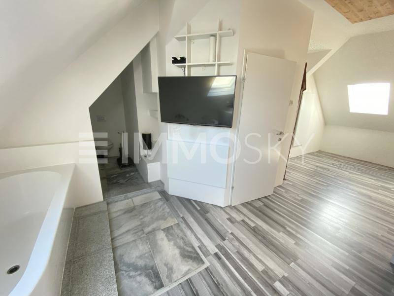 Dachgeschossraum mit Badewanne, Fernseher und schrägen Wänden, modern gestaltet.
