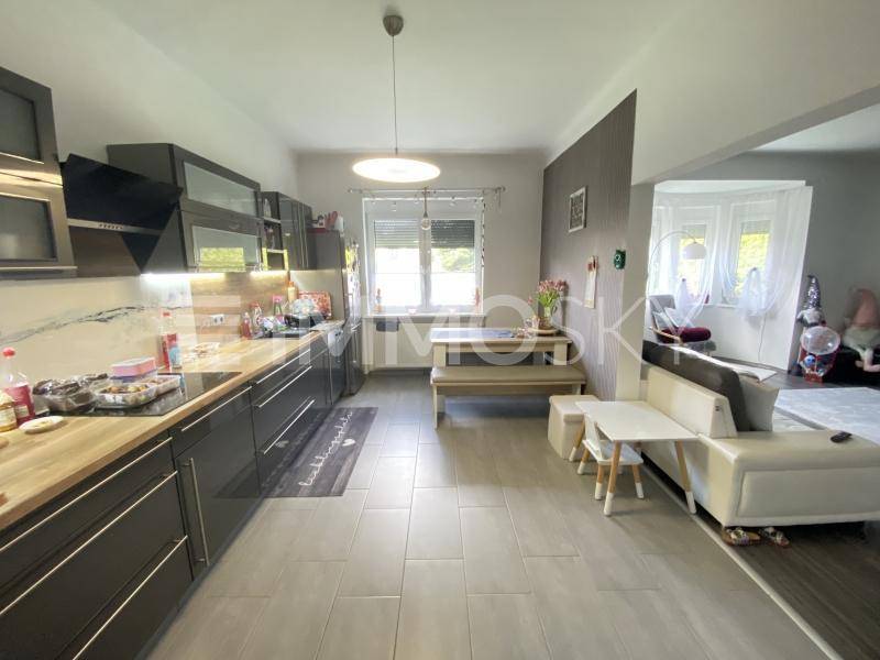 Moderne Küche mit dunklen Schränken, Holzarbeitsplatte und Essbereich, offen zum Wohnzimmer.