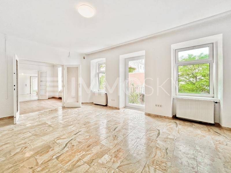 Helles Wohnzimmer mit elegantem Fliesenboden und großen Fenstern mit Blick ins Grüne.
