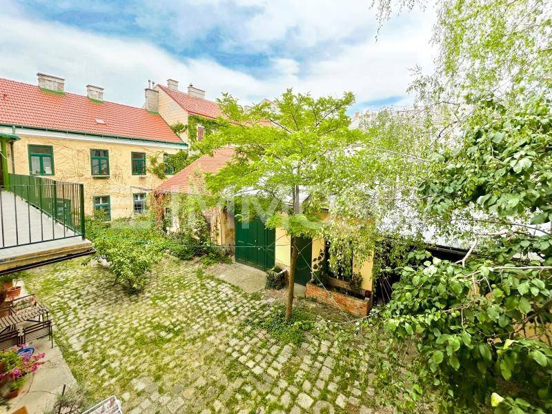 Grüner Innenhof mit Kopfsteinpflaster und Bäumen, umgeben von historischen Gebäuden.