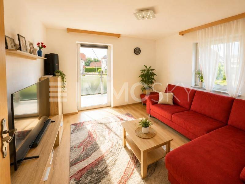 Gemütliches Wohnzimmer mit rotem Ecksofa, Laminatboden und Zugang zu einer Terrasse oder Garten.