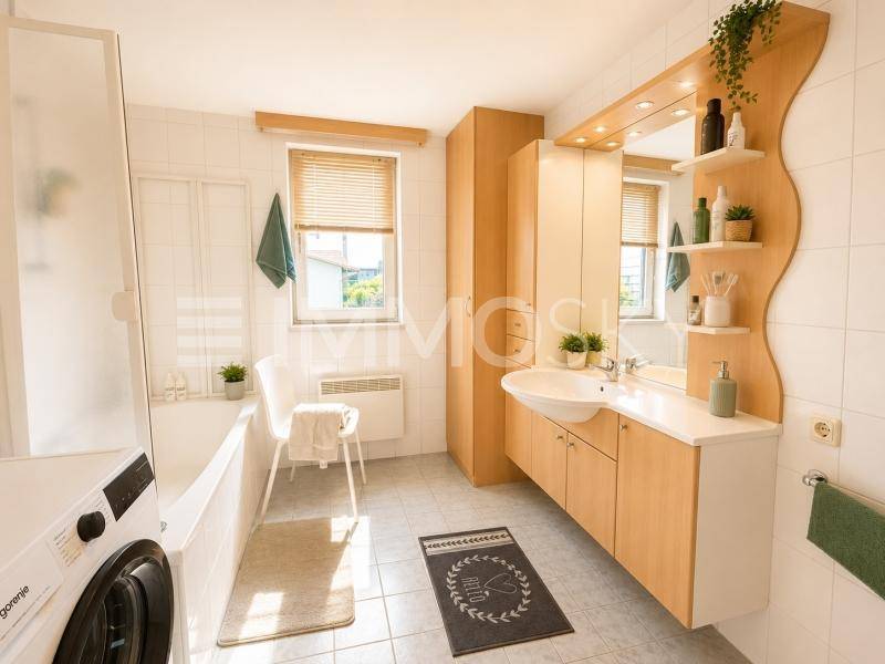 Helles Badezimmer mit Badewanne, Waschbeckenunterschrank, Waschmaschine und Fenster.