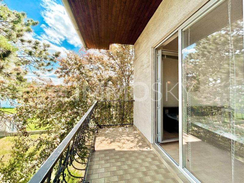 Sonniger Balkon mit schmiedeeisernem Geländer, Fliesenboden und Blick ins Grüne.