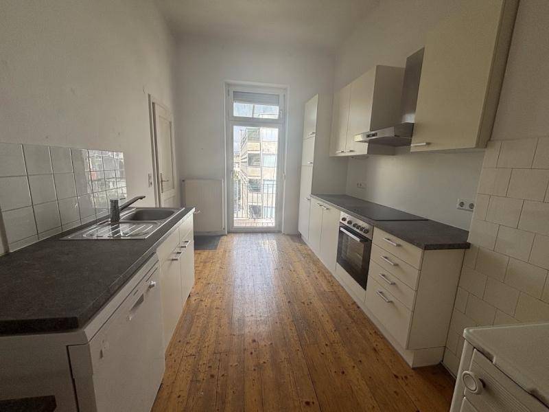 Funktionale Küche mit hellen Schränken, dunklen Arbeitsplatten, Holzfußboden und Zugang zu einem kleinen Balkon.