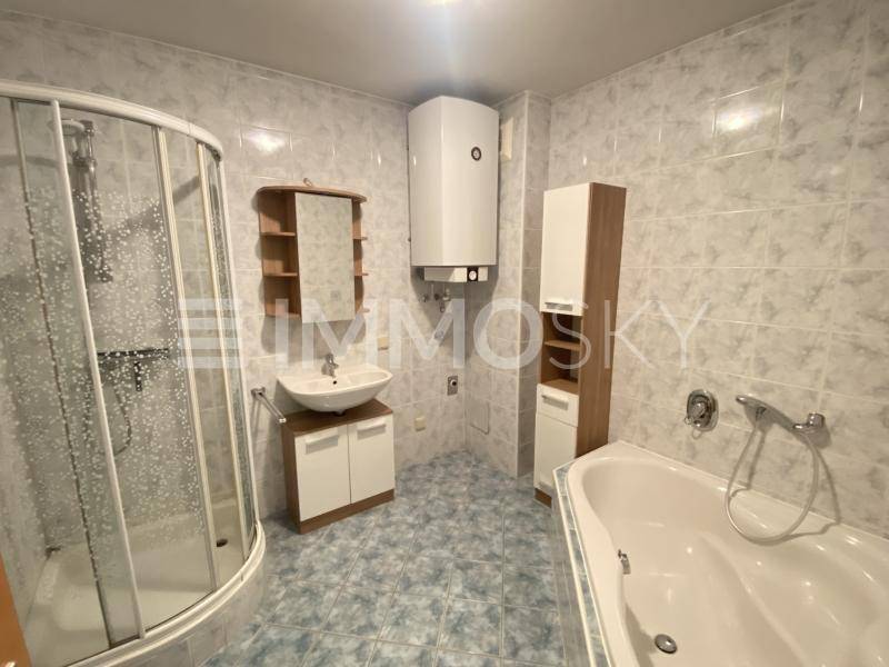 Gefliestes Badezimmer mit Duschkabine, Badewanne, Waschbecken und einem Warmwasserboiler.