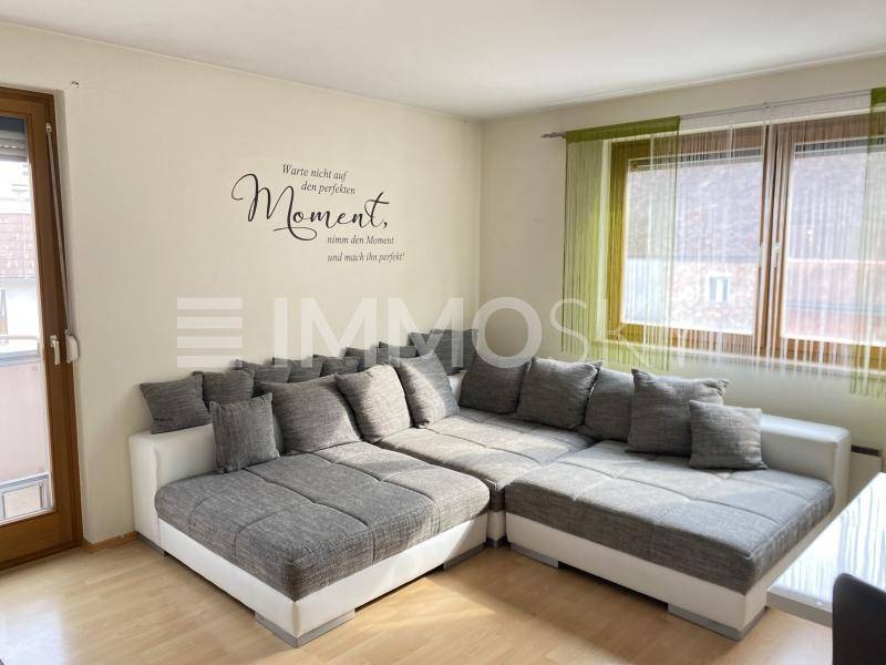 Gemütliches Ecksofa im Wohnbereich mit dekorativem Wandtattoo und Blick auf die Fenster mit Jalousien.