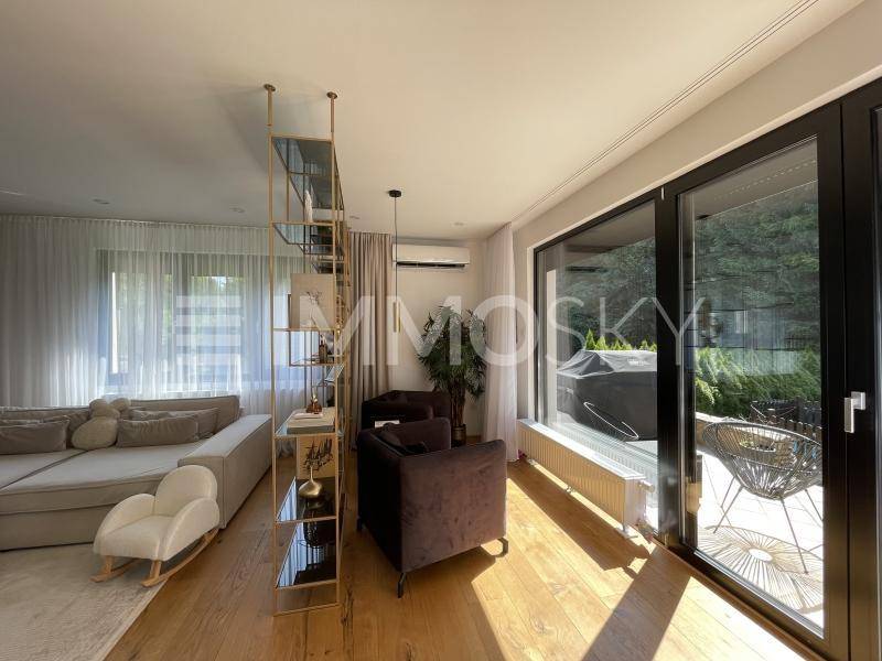 Helles Wohnzimmer mit Holzboden, großen Fenstern und Zugang zum Außenbereich.