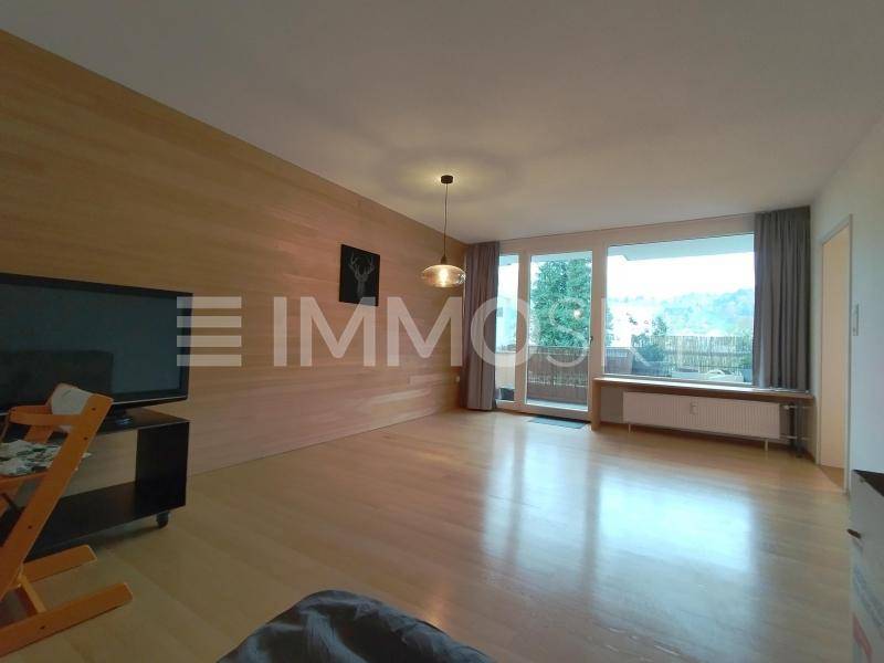 Helles Wohnzimmer mit Holzwand, Parkettboden und direktem Zugang zum Balkon.