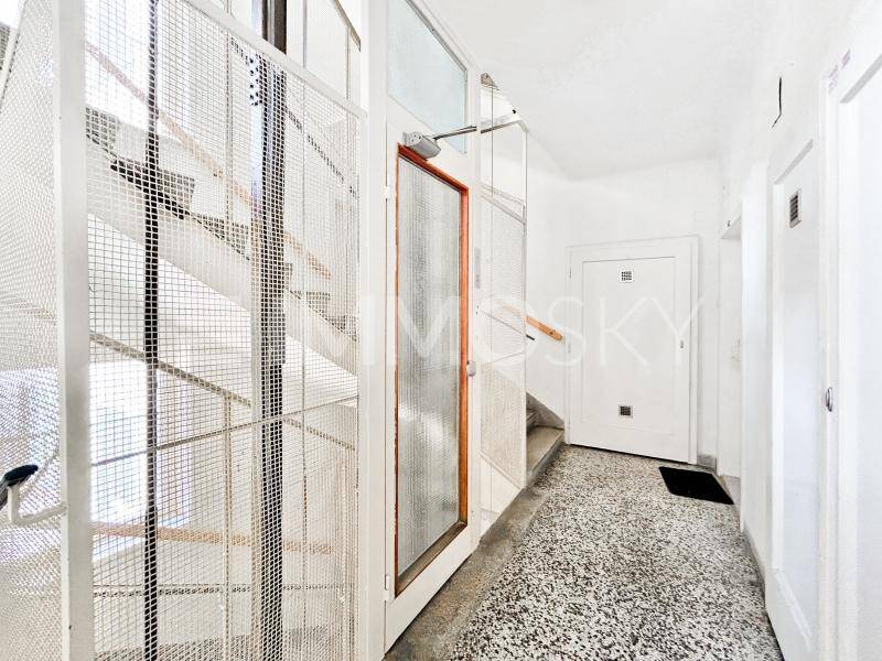 Heller Treppenaufgang mit Terrazzoboden und einem Gitteraufzug in einem Mehrfamilienhaus.