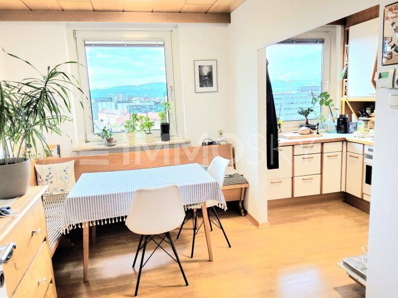 Gemütliche Wohnküche mit Essbereich am Fenster und Blick auf die Stadt.