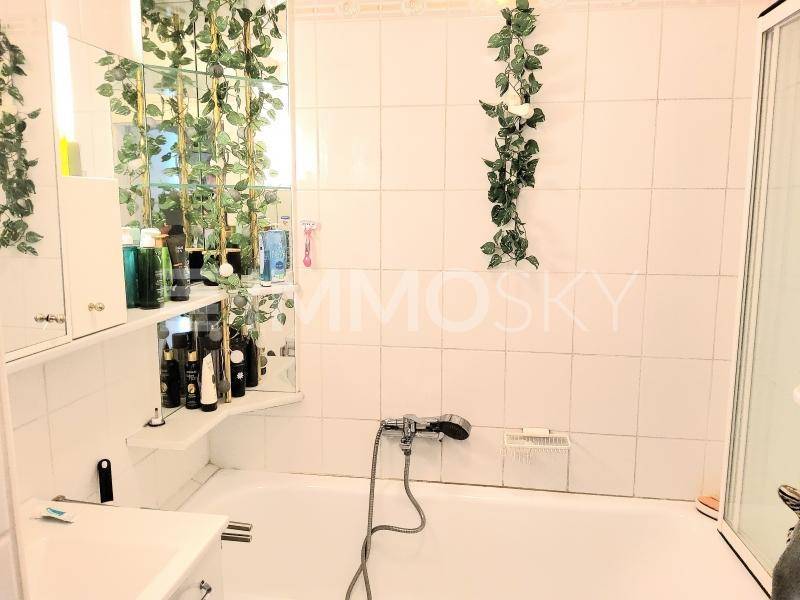 Badezimmer mit weißen Fliesen, Badewanne und einem Spiegelschrank, dekoriert mit Pflanzen.