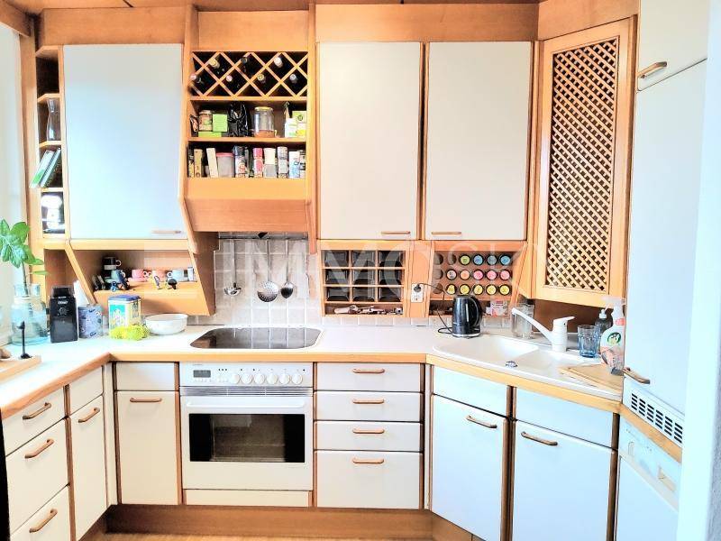 Funktionale Küche mit hellen Holzschränken, integriertem Backofen und Weinregal.