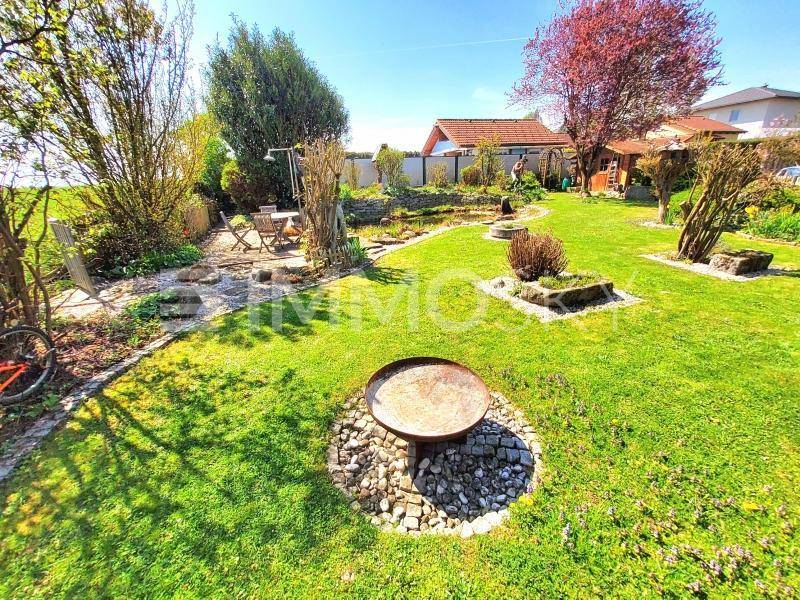 Weitläufiger Garten mit einer Feuerstelle, einem Teich und einer kleinen Sitzecke im Sonnenlicht.