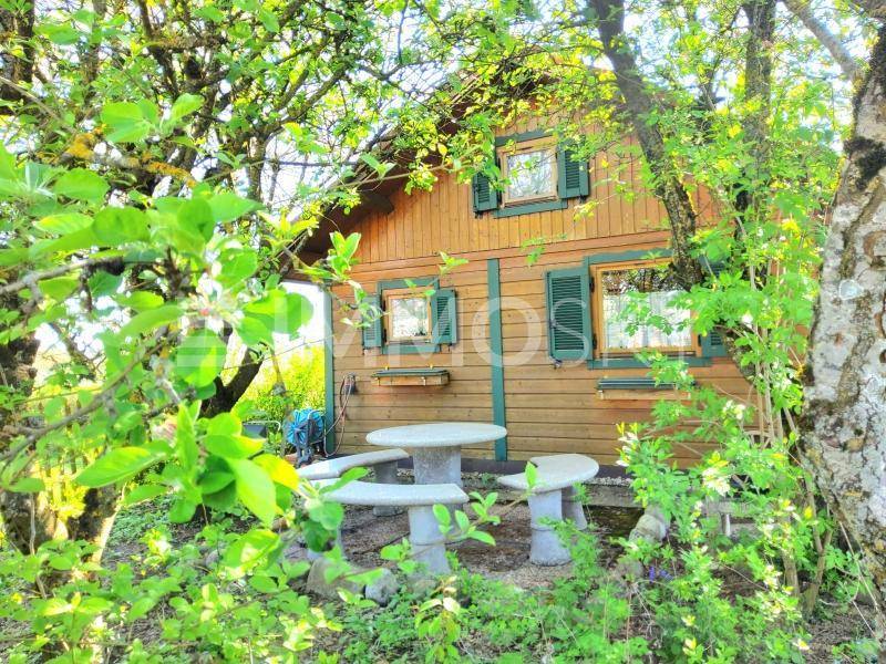 Rustikales Holzhaus umgeben von Bäumen mit einem kleinen Steintisch und Bänken im Freien.