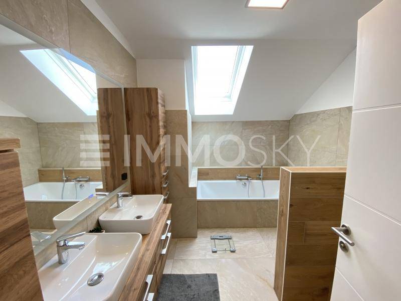 Modernes Badezimmer mit Doppelwaschbecken, Badewanne und Dachfenster für natürliches Licht.