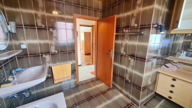 Badezimmer mit braunen Fliesen an Wänden und Boden, einem rosafarbenen Waschbecken und Holzunterschrank.