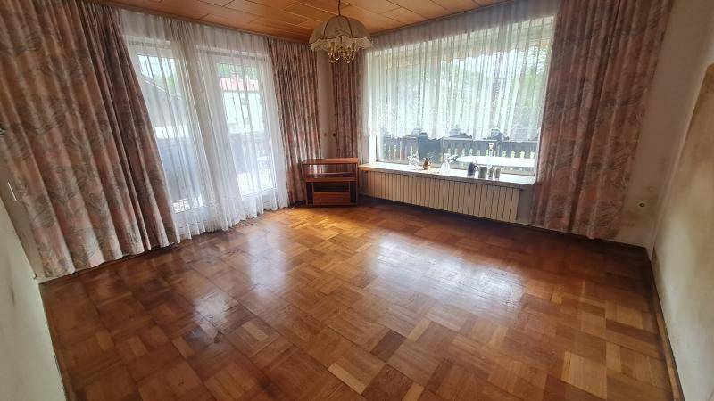 Wohnzimmer mit Parkettboden, Holzdecke und großen Fenstern mit Vorhängen, die viel Licht spenden.