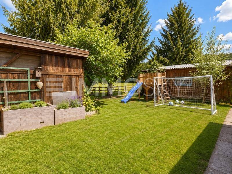 Gepflegter Gartenbereich mit Rasenfläche, Spielgeräten für Kinder und einem praktischen Gartenhaus.