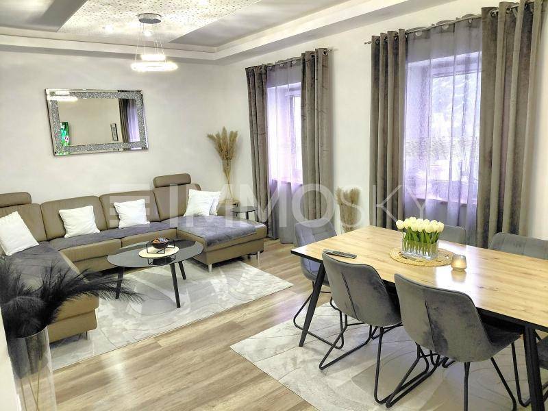 Moderner Wohn- und Essbereich mit beigem Sofa, Holzboden und stilvoller Deckenbeleuchtung.