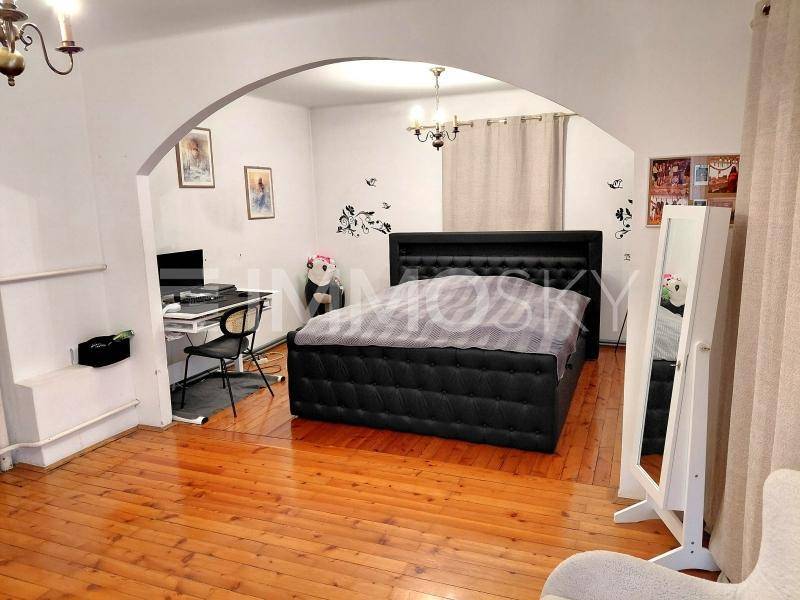Schlafzimmer mit großem Doppelbett, Schreibtisch und Holzboden, verbunden durch einen Bogen.