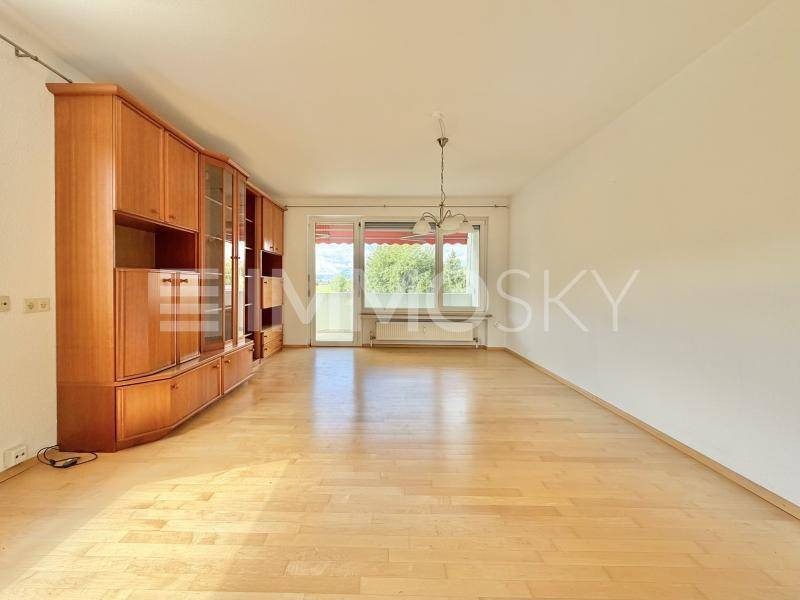 Helles Wohnzimmer mit Parkettboden, großem Holzschrank und Zugang zum Balkon.