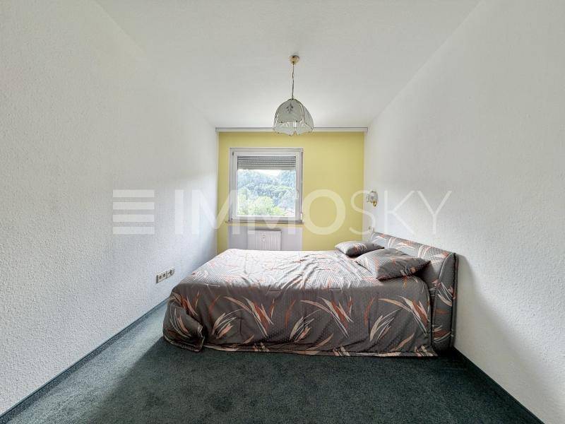Schlafzimmer mit Teppichboden, Bett und Fenster mit Blick ins Grüne.