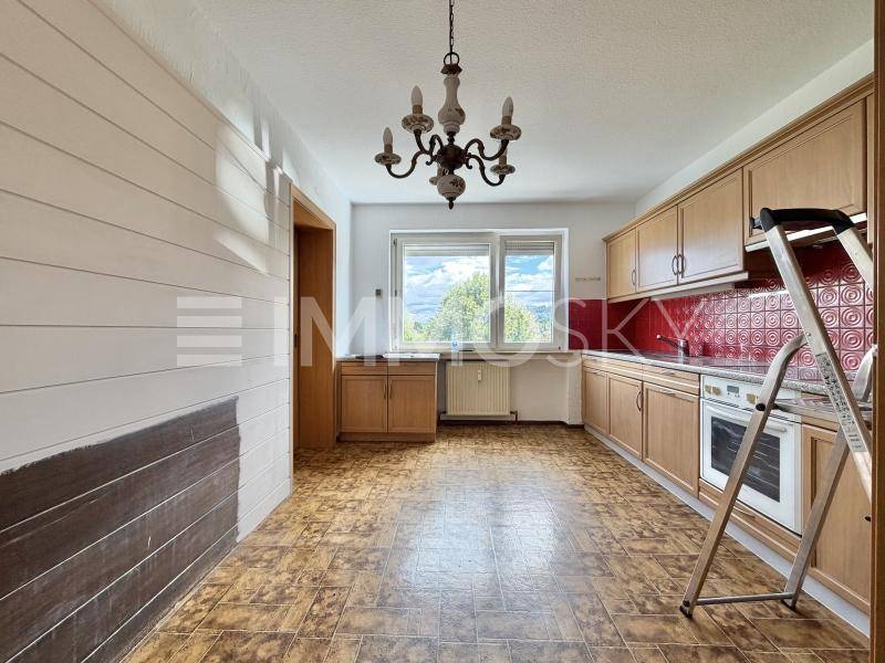 Küche mit älterem Vinylboden, Holzschränken und Fensterblick ins Grüne.