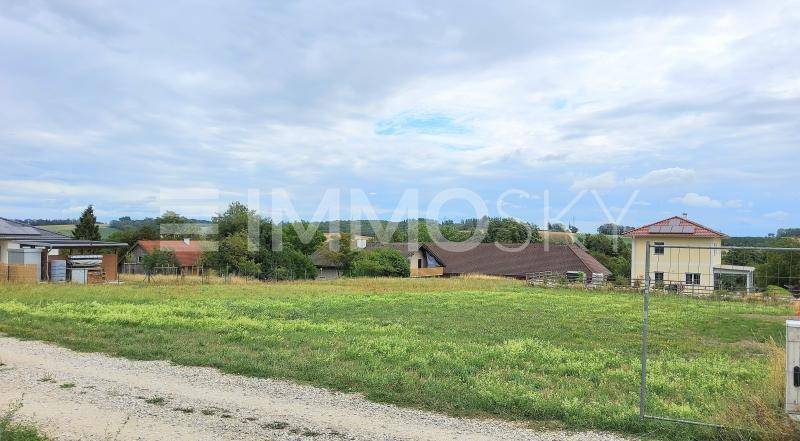 Offenes Feld mit mehreren Wohnhäusern in der Ferne unter einem bewölkten Himmel.