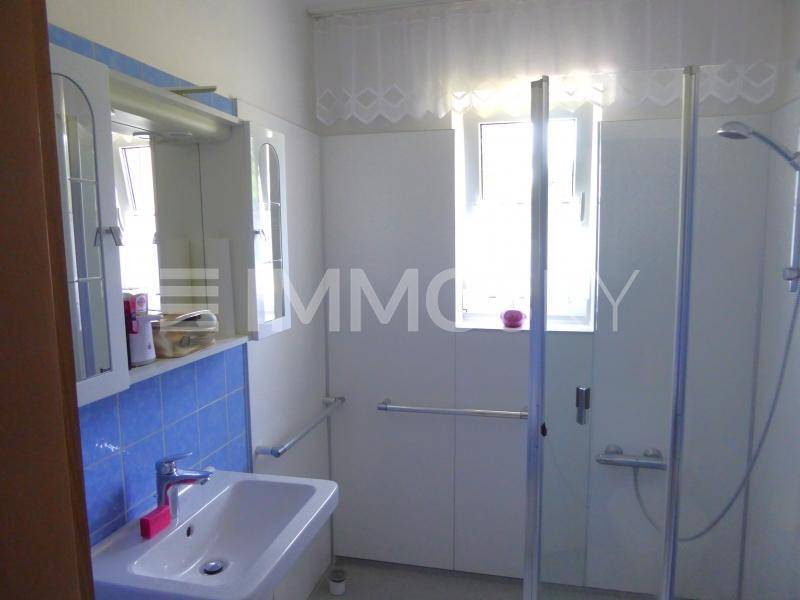 Badezimmer mit Dusche, Waschbecken, Spiegelschrank und zwei Fenstern für Tageslicht.