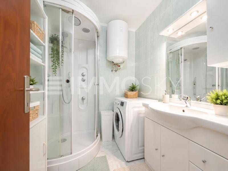Badezimmer mit Duschkabine, Waschbeckenunterschrank und Waschmaschine.