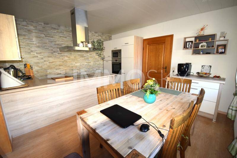 Moderne Wohnküche mit Essbereich, Holztisch und einer Küchenzeile mit Steinoptik-Rückwand.