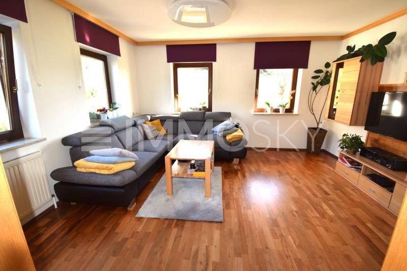 Helles Wohnzimmer mit bequemer grauer Eckcouch, Holzboden und großen Fenstern.