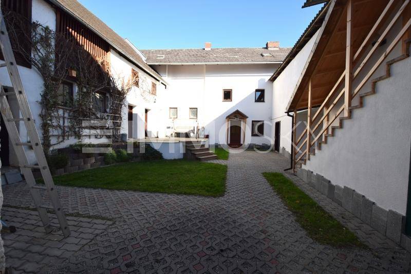 Innenhof mit gepflastertem Bereich und weiß getünchten Gebäudefassaden, umgeben von Grünflächen.