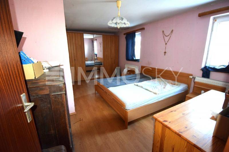 Gemütliches Schlafzimmer mit rosa Wänden, Holzbett, Kleiderschrank mit Spiegeltür und einem Fenster.