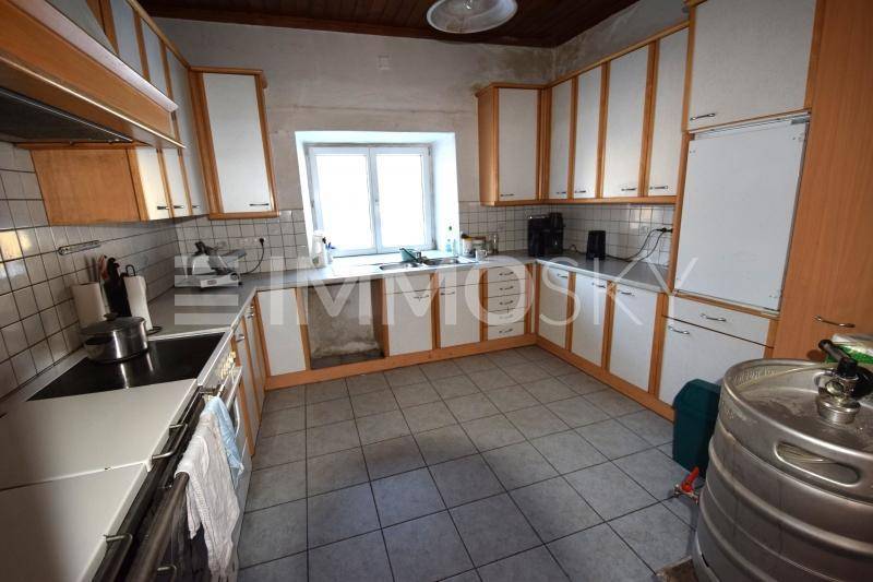 Funktionale Küche mit weißen und holzfarbenen Schränken, Fliesenboden und einem Fenster über der Spüle.