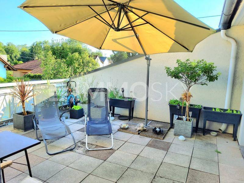 Sonniger Balkon mit Fliesenboden, Sonnenschirm und Pflanzen in Hochbeeten.