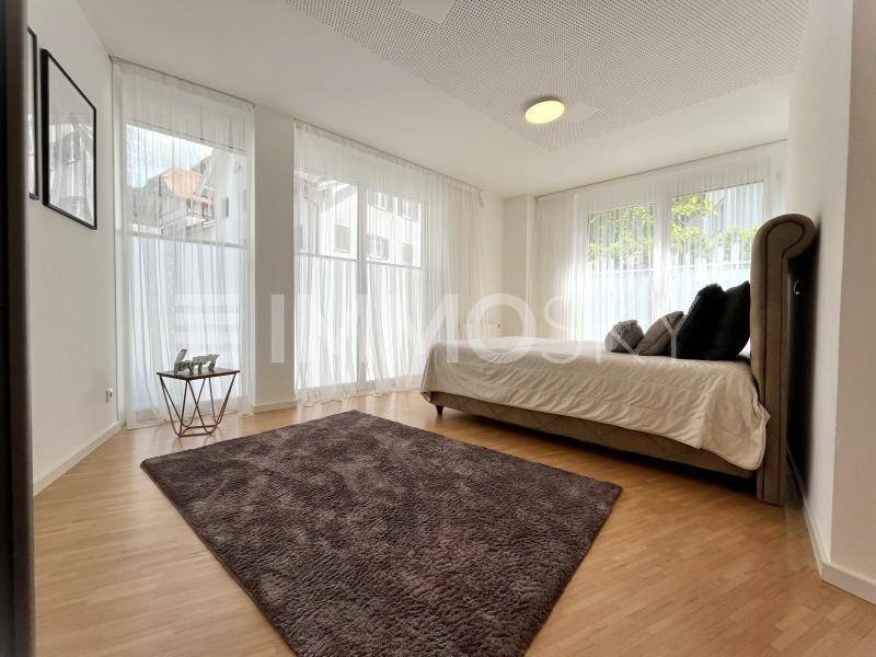 Schlafzimmer mit hellem Holzboden, großen Fenstern und viel Tageslicht.