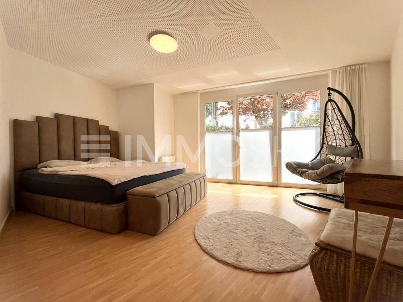 Gemütliches Schlafzimmer mit großem Bett, Hängesessel und Zugang zu großen Fenstern.