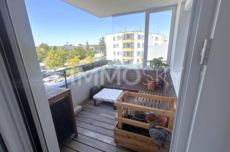 Sonniger Balkon mit Holzboden, Sitzgelegenheiten und Blick auf die Umgebung.