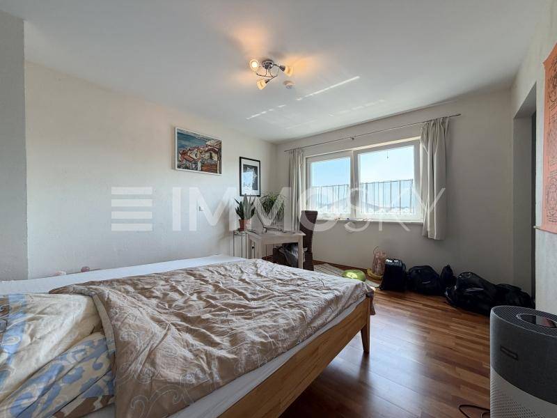 Gemütliches Schlafzimmer mit Holzboden, großem Bett und einem Fenster mit Ausblick ins Freie.