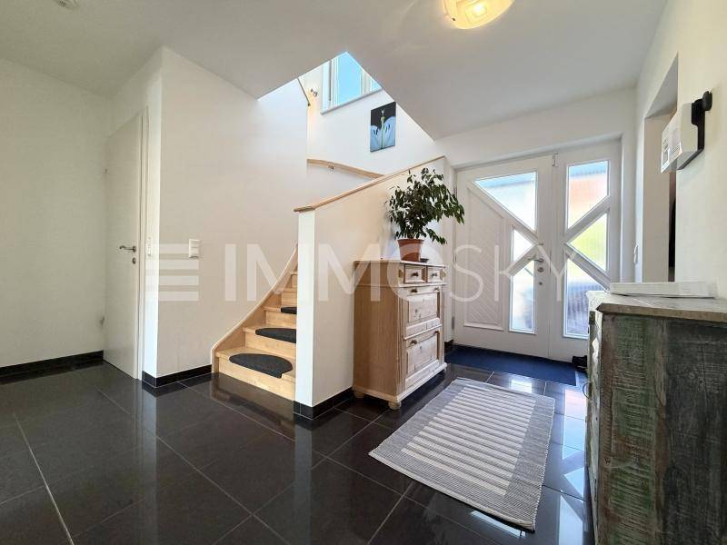 Heller Eingangsbereich mit Treppe, dunklen Fliesen und viel Tageslicht durch die Glastür.